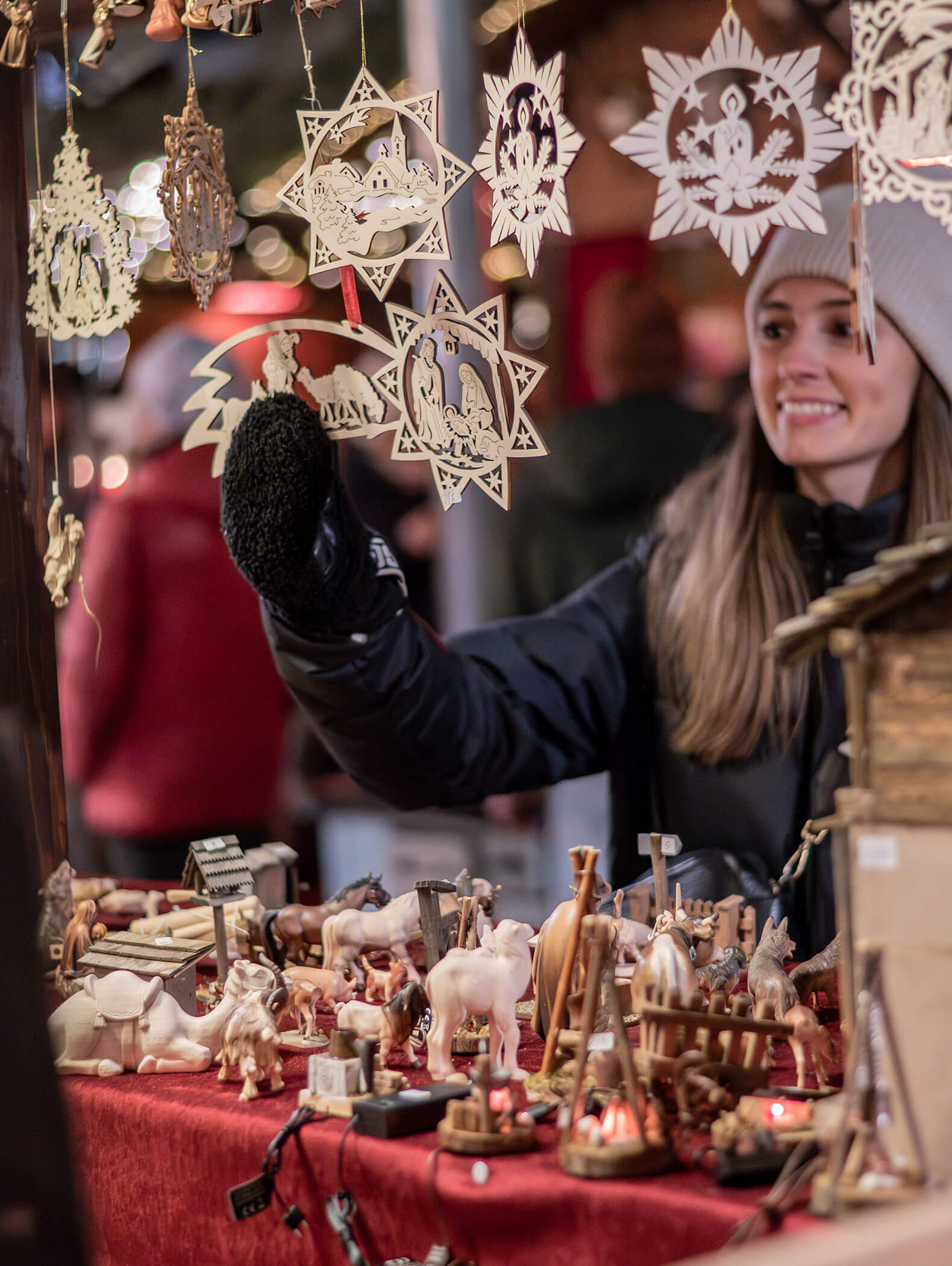 Eine Frau in Winterkleidung bewundert Holzornamente an einem festlichen Marktstand im Freien. - Hotel B&B MyLiving