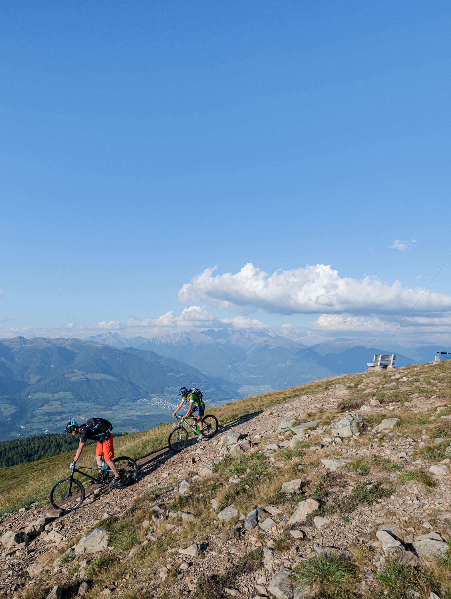Zwei Mountainbiker fahren bergauf auf einem felsigen Weg mit Bergen und blauem Himmel im Hintergrund. - Hotel B&B MyLiving