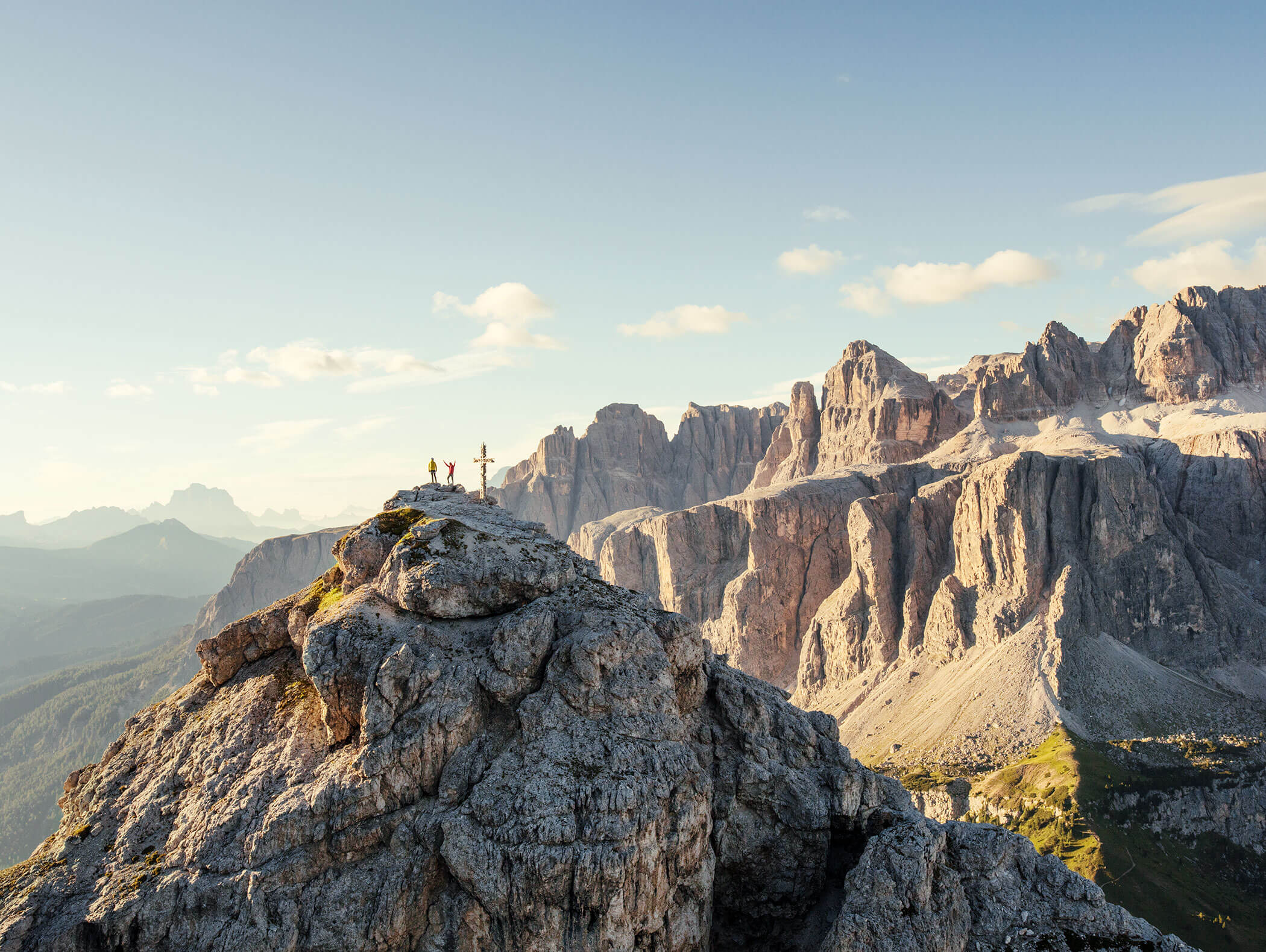 Drei Wanderer stehen bei einem Kreuz auf einem felsigen Berggipfel mit dramatischen Klippen im Hintergrund. - Hotel B&B MyLiving