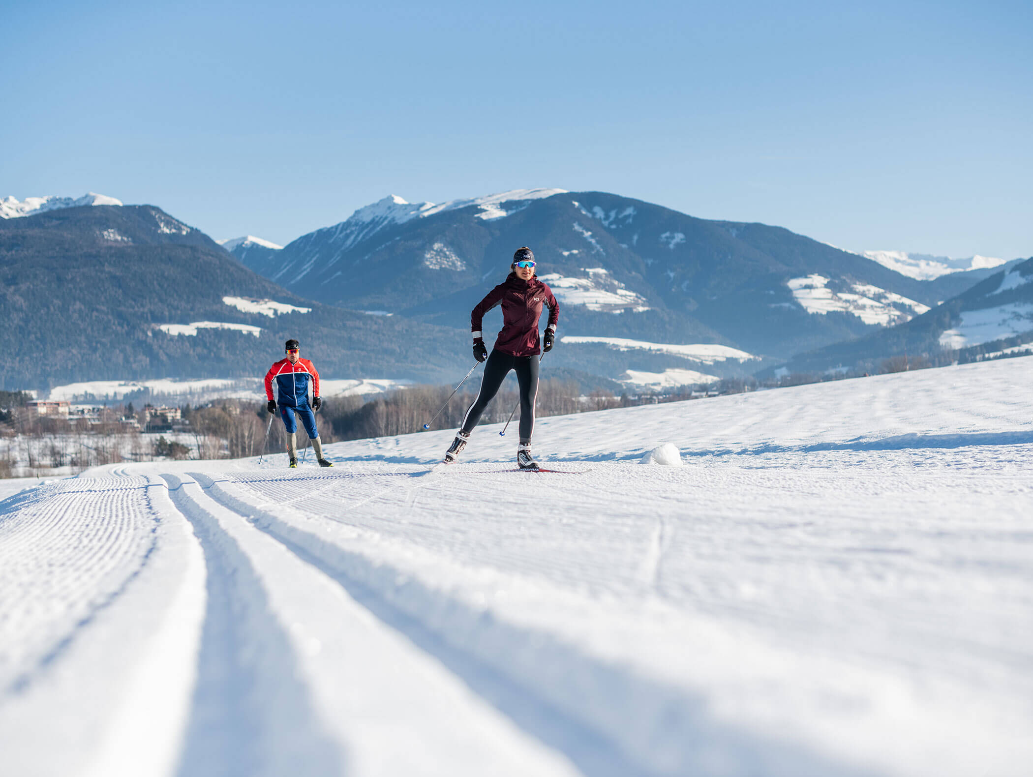 Zwei Personen beim Skilanglauf auf einer verschneiten Loipe mit Bergen im Hintergrund an einem klaren Tag. - Hotel B&B MyLiving