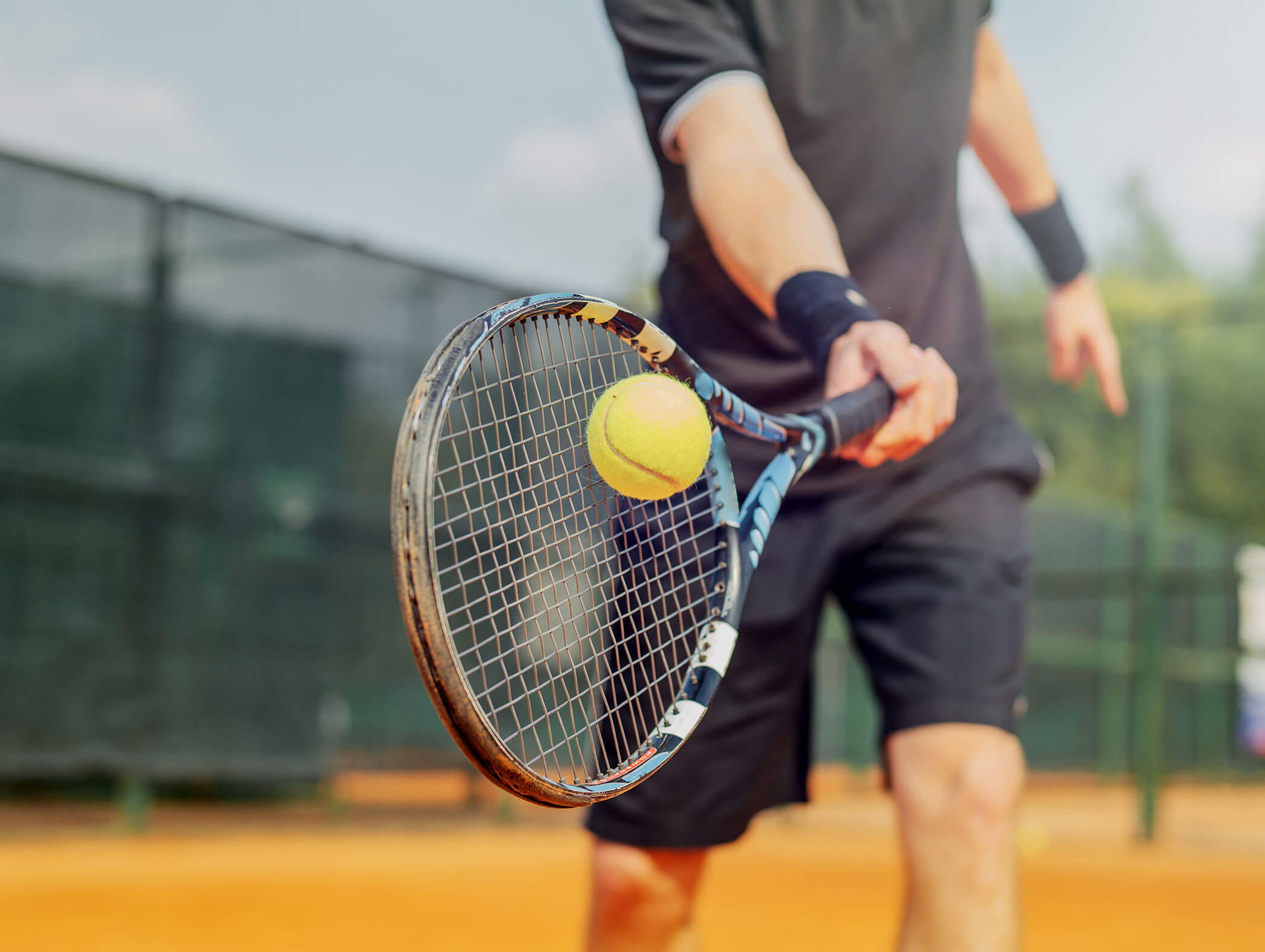 Nahaufnahme eines Tennisspielers, der einen Tennisball mit einem Schläger auf einem Sandplatz im Freien schlägt. - Hotel B&B MyLiving