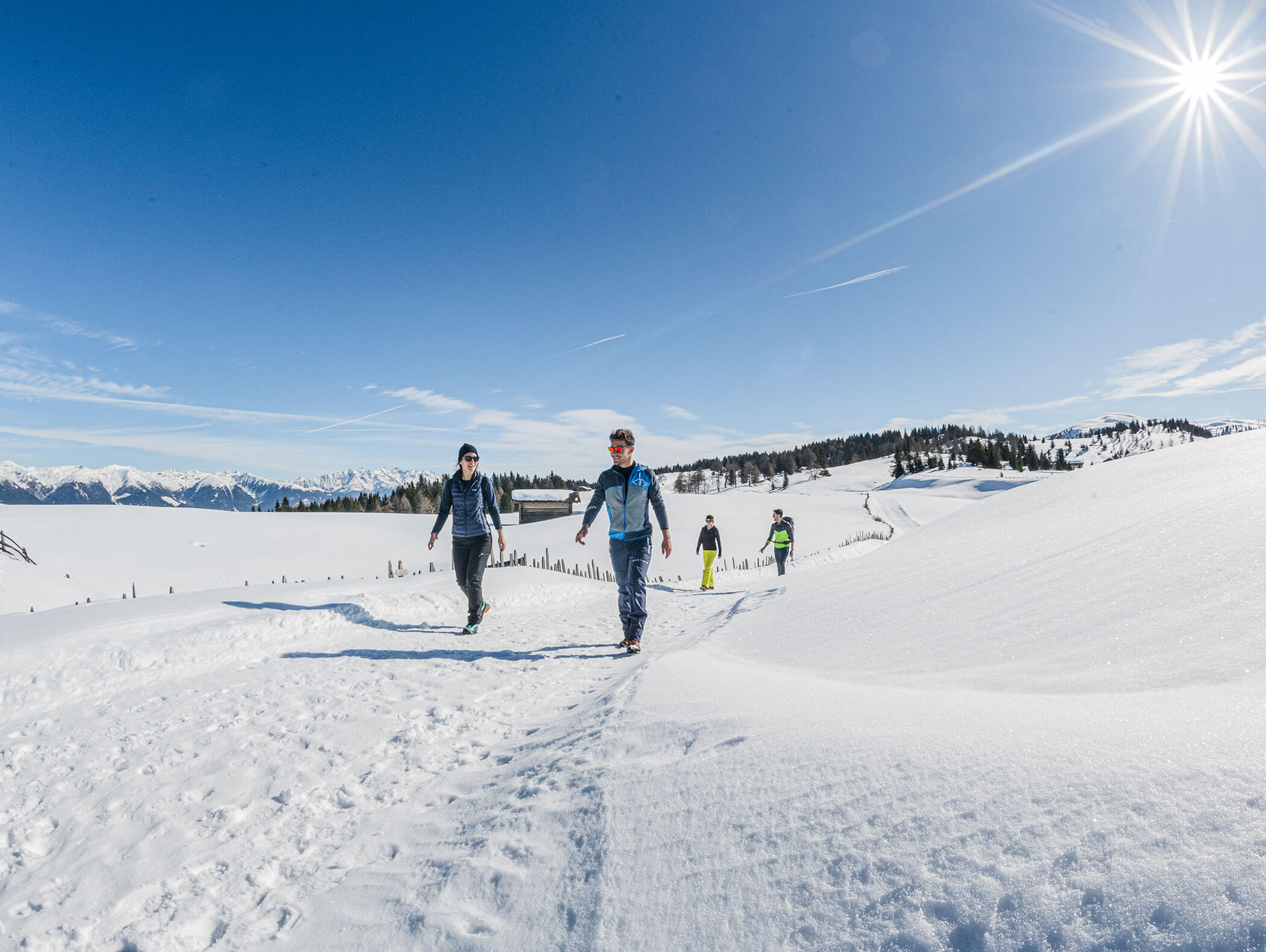 Zwei Personen wandern auf einem verschneiten Bergpfad bei strahlendem Sonnenschein, andere folgen ihnen. - Hotel B&B MyLiving