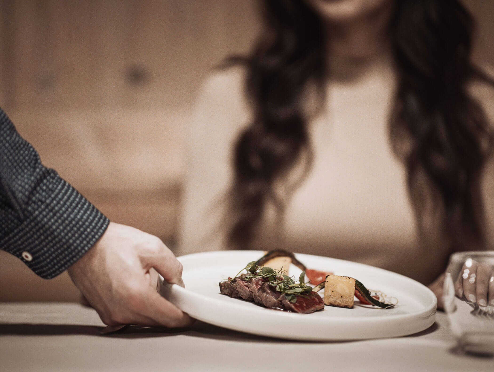 Ein Kellner reicht einer Frau, die an einem Tisch in einem Restaurant sitzt, einen Teller mit Gourmetgerichten. - Hotel B&B MyLiving