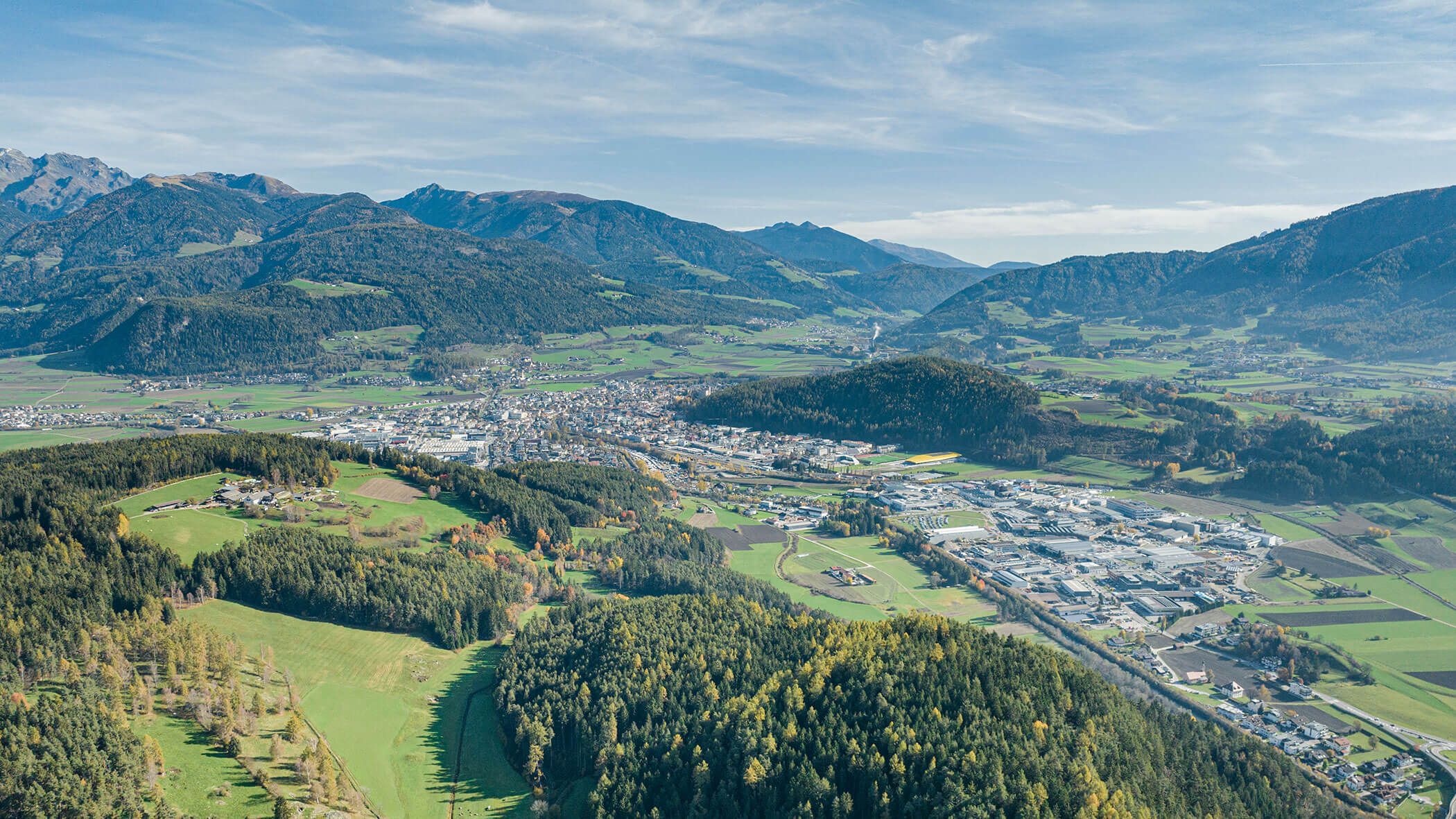 Luftaufnahme einer Stadt, umgeben von grünen Feldern, Wäldern und Bergen unter blauem Himmel. - Hotel B&B MyLiving