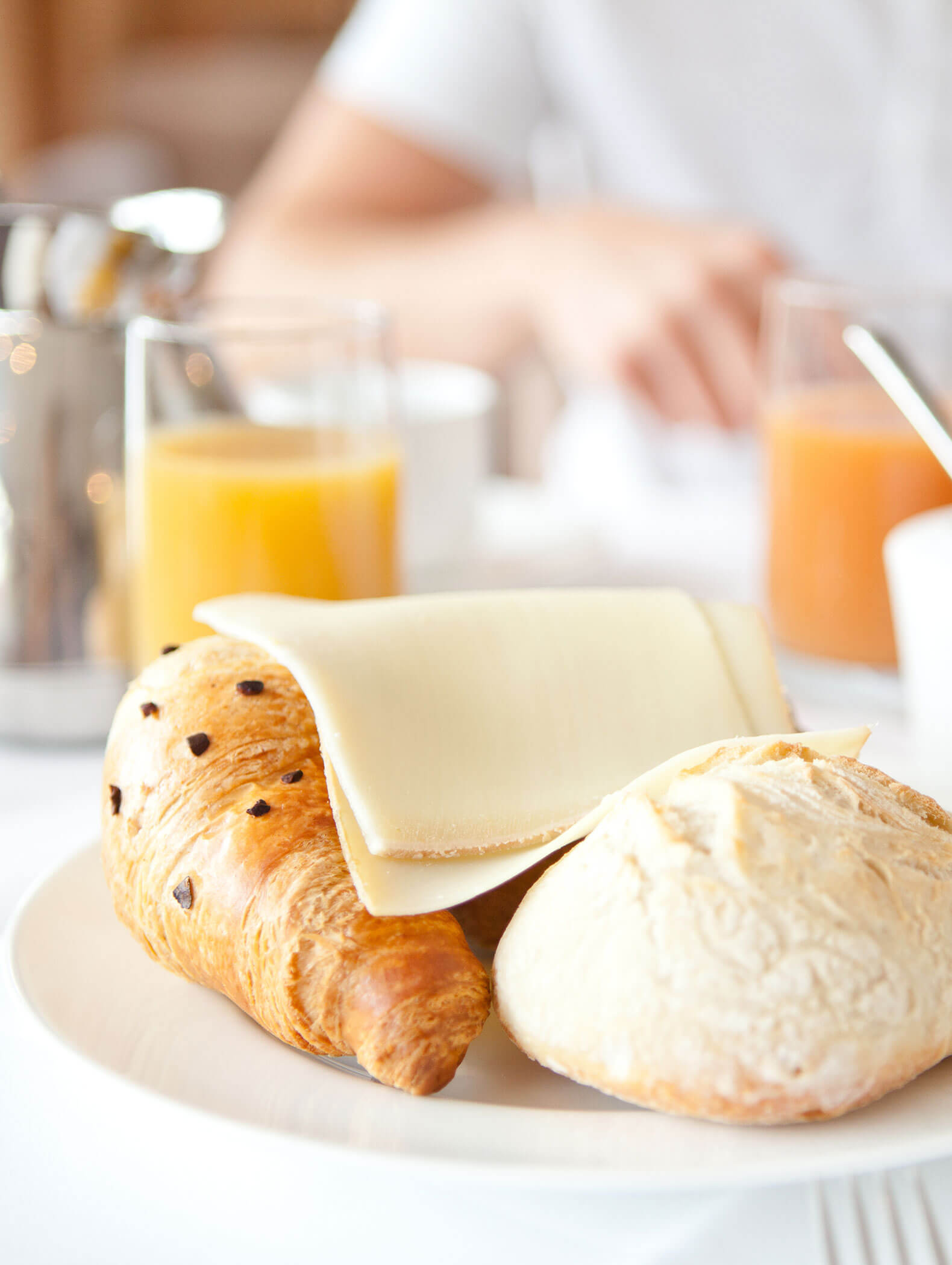 Ein Teller mit einem Croissant, einem Brötchen und Käsescheiben; im Hintergrund steht Orangensaft. - Hotel B&B MyLiving
