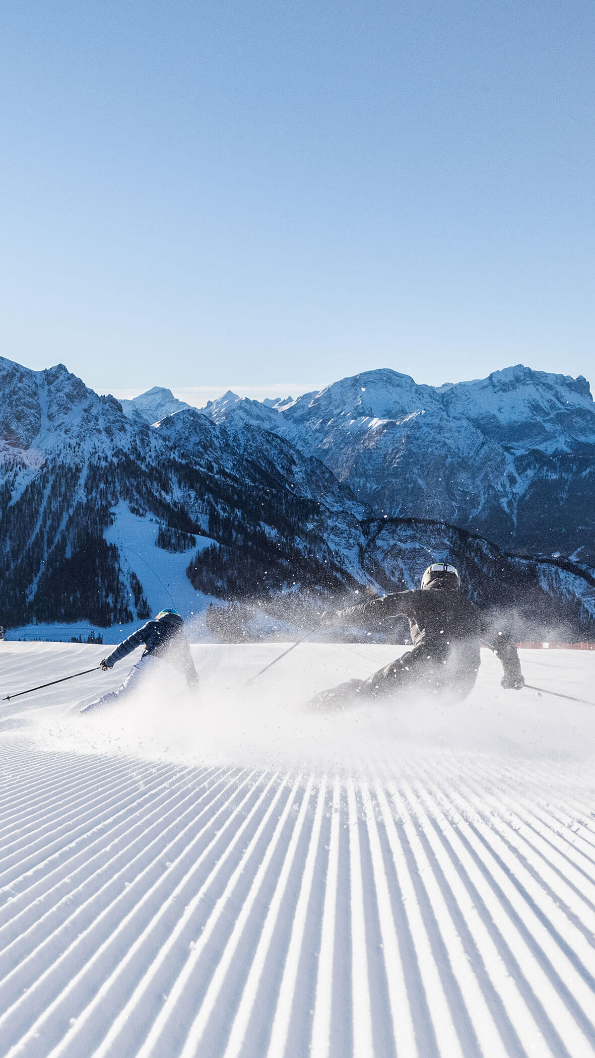 Ein Snowboarder carvt durch frischen Schnee auf einer präparierten Piste mit Bergen im Hintergrund. - Hotel B&B MyLiving