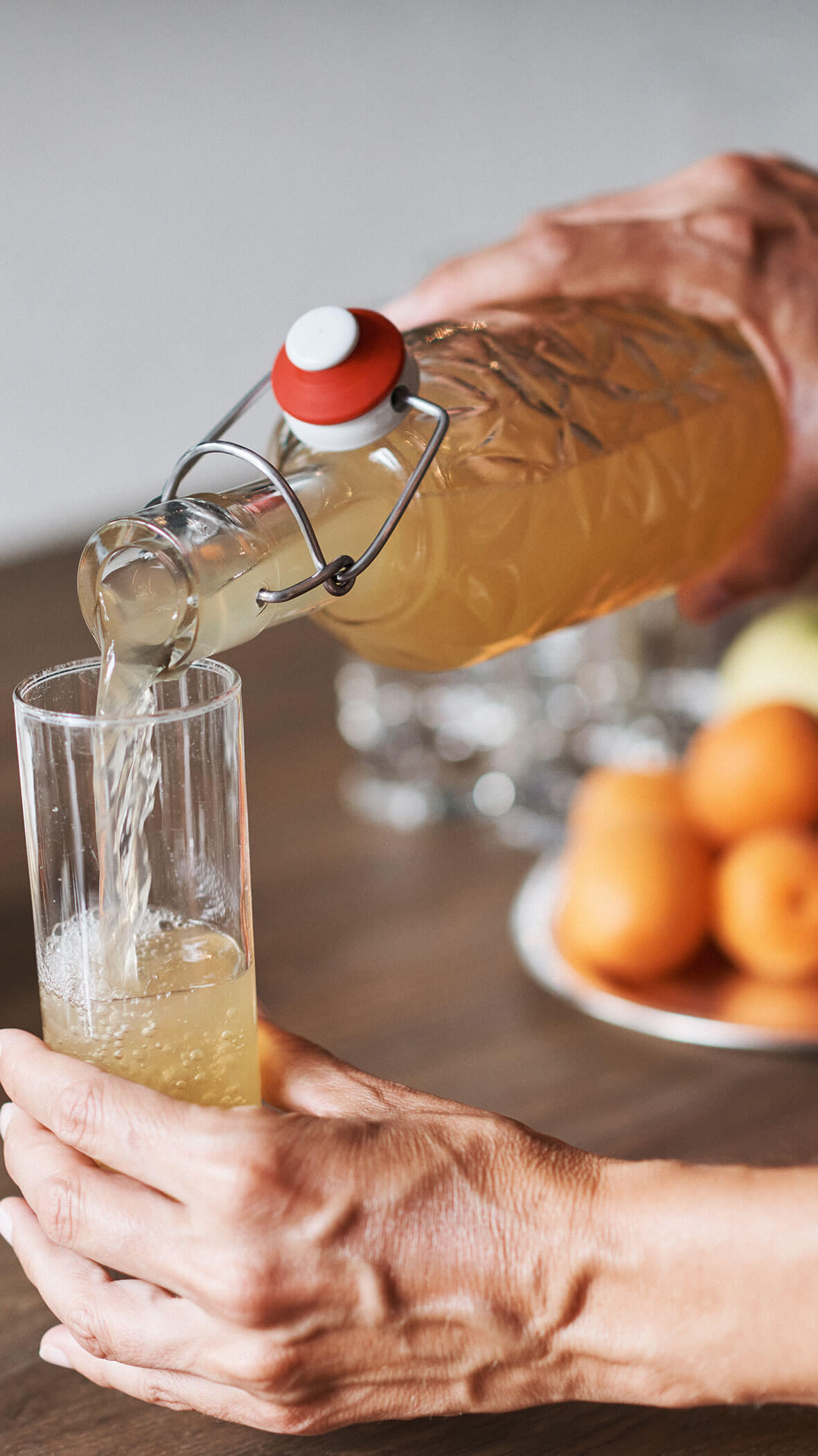 Eine Person gießt ein helles Getränk aus einer Glasflasche in ein hohes Glas. - Hotel B&B MyLiving