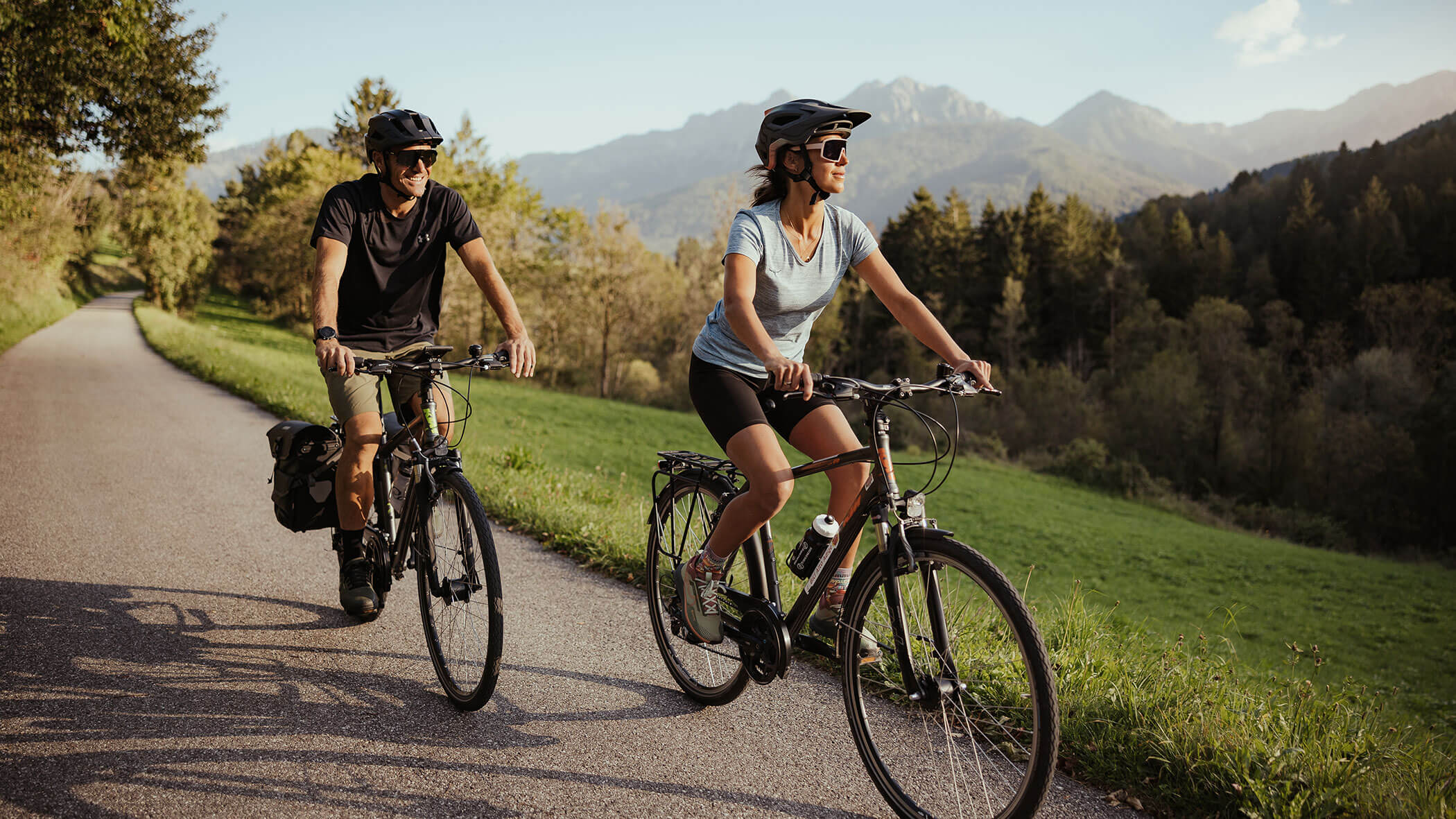 Zwei Personen fahren mit dem Fahrrad auf einer malerischen Landstraße mit Bergen und Bäumen im Hintergrund. - Hotel B&B MyLiving