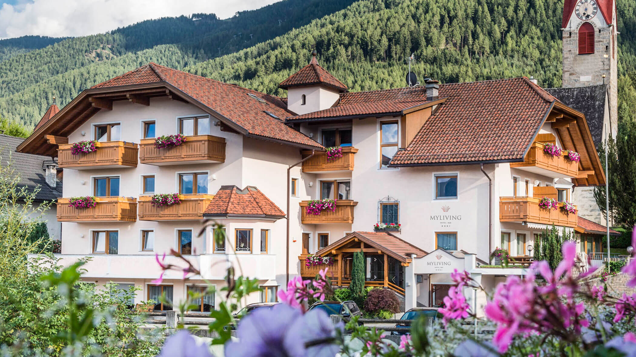 Ein charmantes Alpenhotel mit Holzbalkonen und Blumenkästen inmitten einer bewaldeten Bergkulisse. - Hotel B&B MyLiving