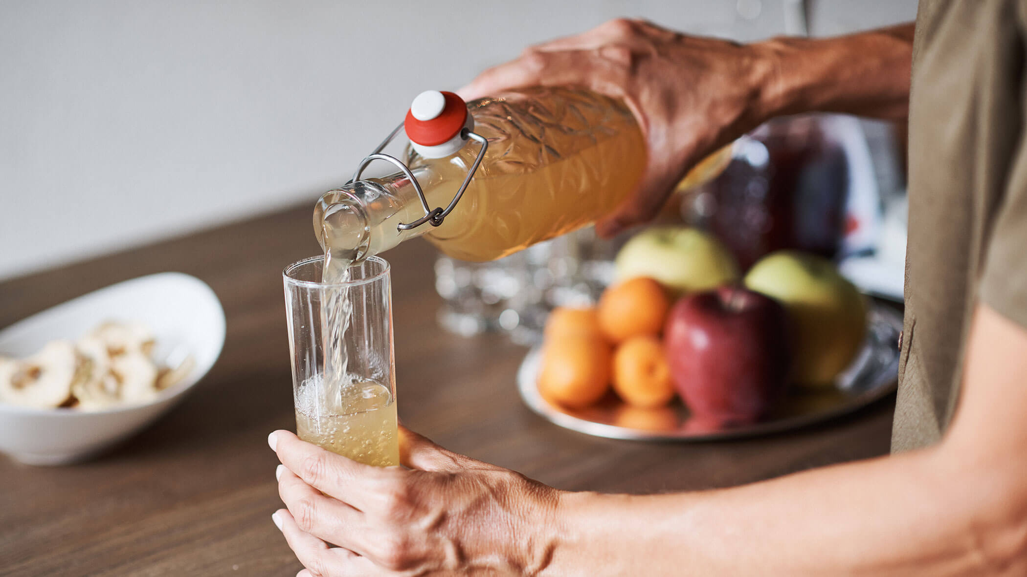 Eine Person gießt ein helles Getränk in ein Glas, während im Hintergrund Früchte auf einem Tablett liegen. - Hotel B&B MyLiving
