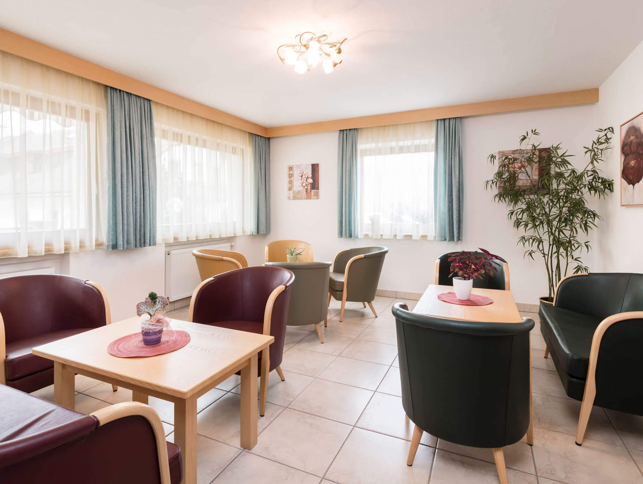 Ein helles Wohnzimmer mit Sesseln, kleinen Tischen, Topfpflanzen und großen Fenstern mit Vorhängen. - Hotel B&B MyLiving