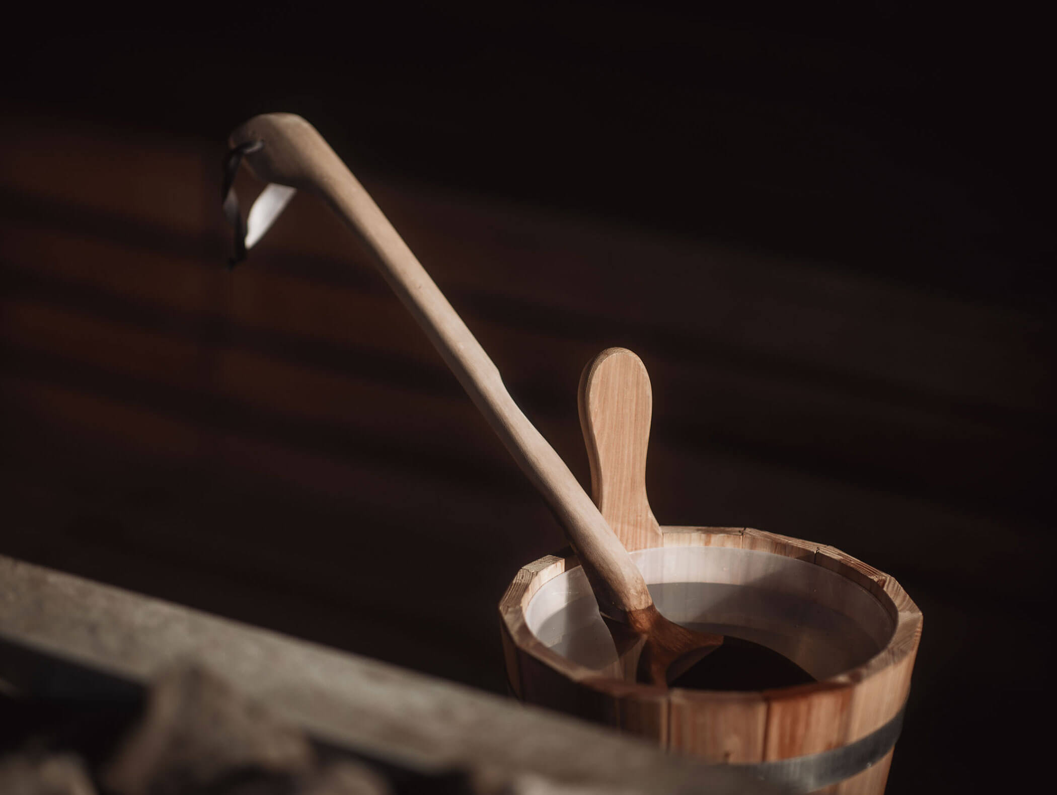 Eine hölzerne Saunakelle, die in einem Holzeimer ruht, mit einem dunklen, unscharfen Hintergrund. - Hotel B&B MyLiving