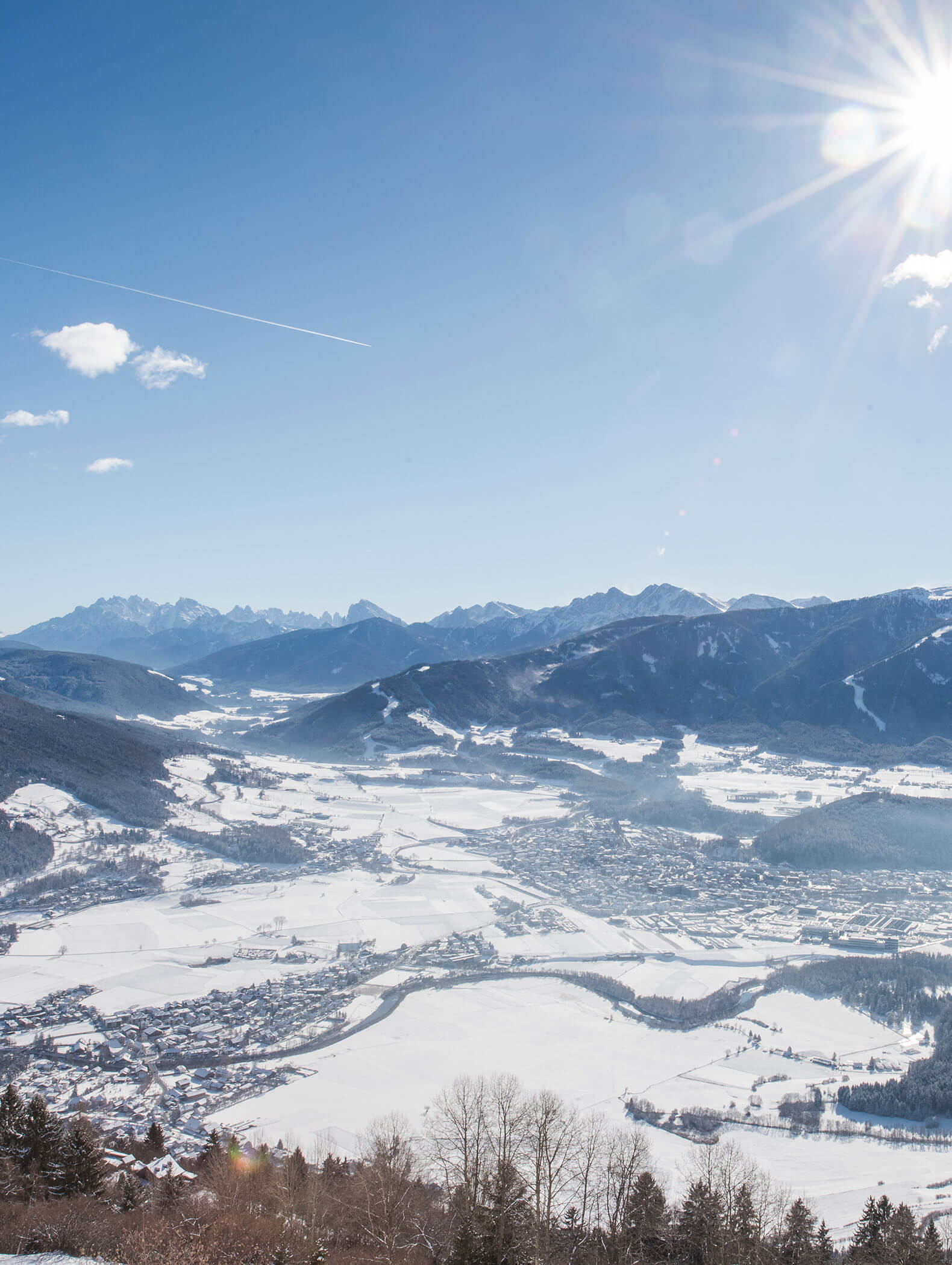 Ein schneebedecktes Tal und eine Stadt mit entfernten Bergen bei strahlendem Sonnenschein und einem sichtbaren Kondensstreifen eines Flugzeugs. - Hotel B&B MyLiving