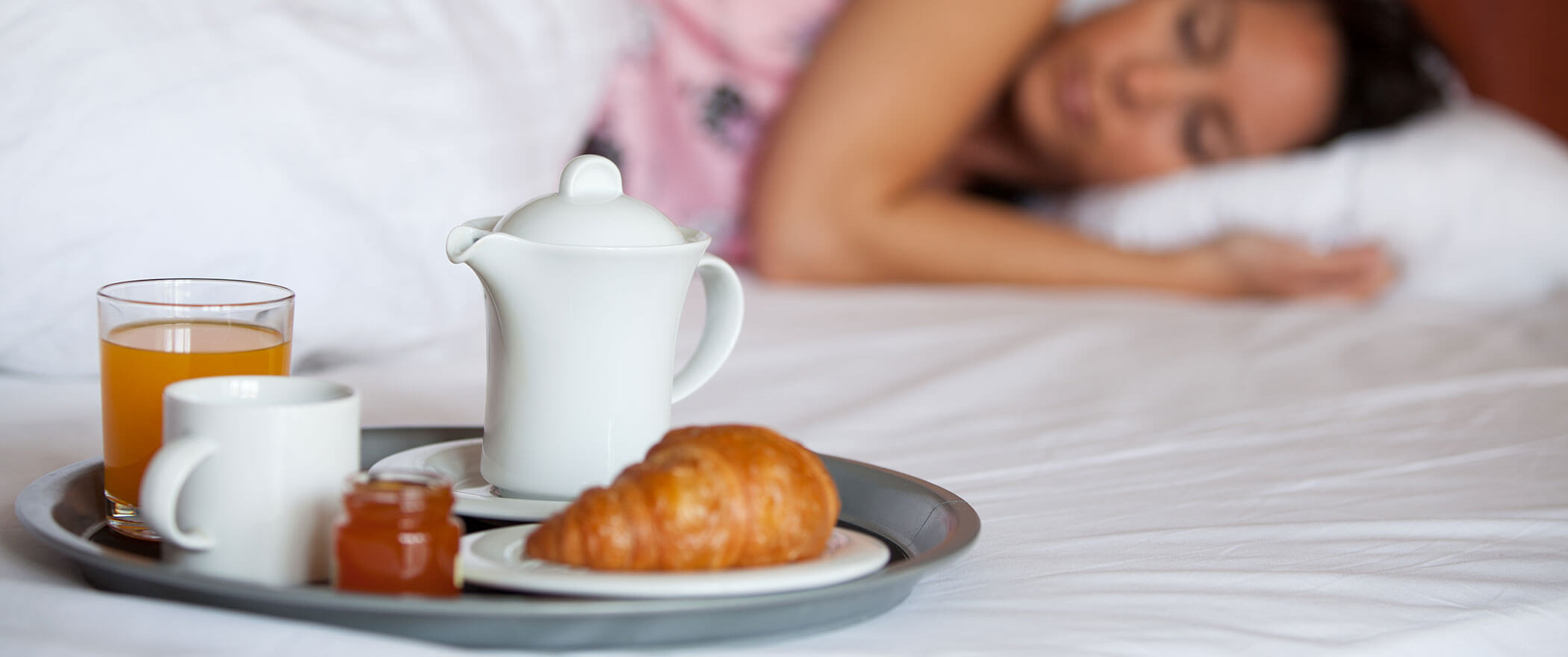 Ein Tablett mit Kaffee, Orangensaft, einem Croissant und Marmelade auf einem Bett neben einer schlafenden Frau. - Hotel B&B MyLiving