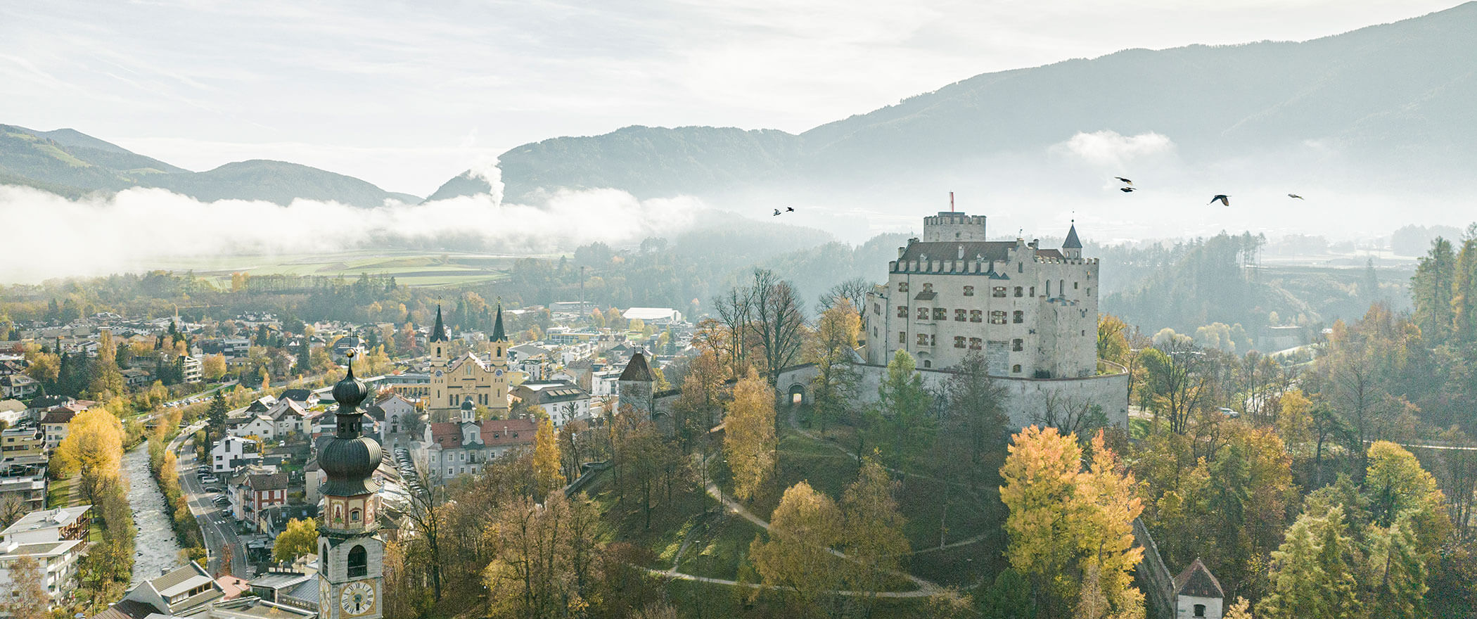 Luftaufnahme eines Schlosses auf einem Hügel mit Herbstbäumen, einer Stadt und Bergen im Hintergrund. - Hotel B&B MyLiving